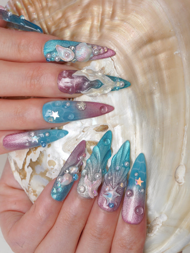 Long stiletto press-on nails with shimmering blue and pink gradients, 3D seashells, starfish, and pearl details
