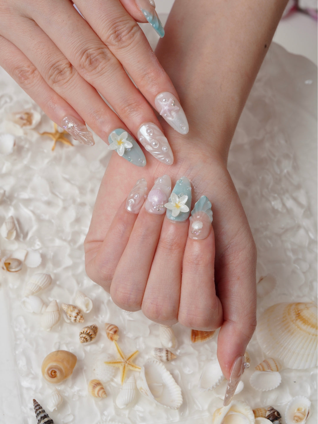 Handmade beach-themed nails featuring soft nude, blue, and white tones with seashell and floral details