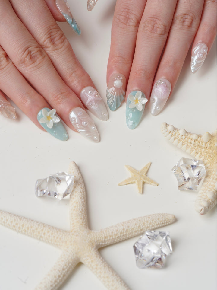 Handmade beach-themed nails featuring soft nude, blue, and white tones with seashell and floral details