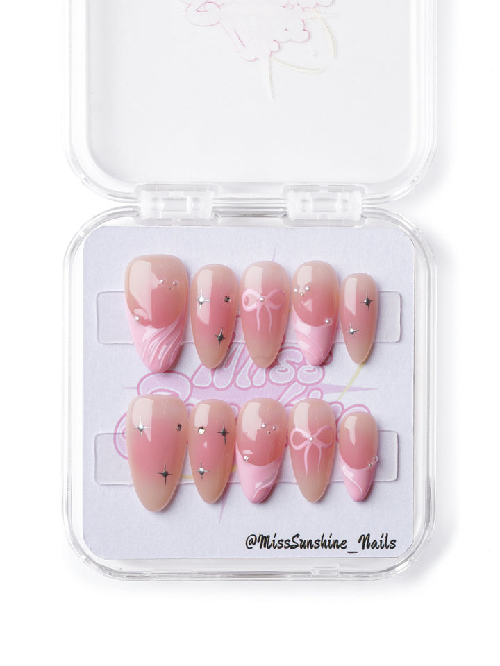 Elegant soft pink short almond press-on nails with dainty bows, shimmering accents, and a ballet-inspired ombré design.