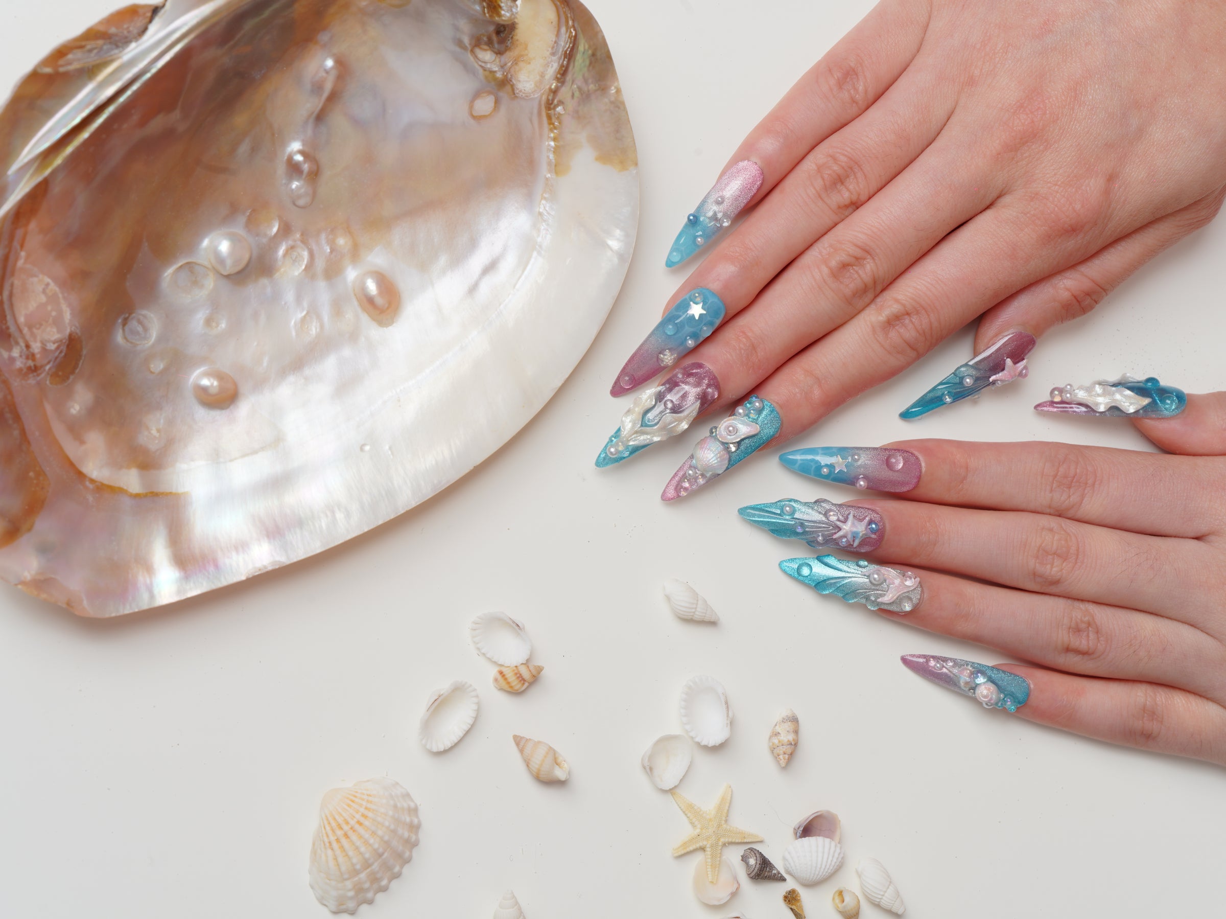 Long stiletto press-on nails with pastel ocean gradients, 3D starfish and shells, pearl details, and mermaid-inspired shimmer