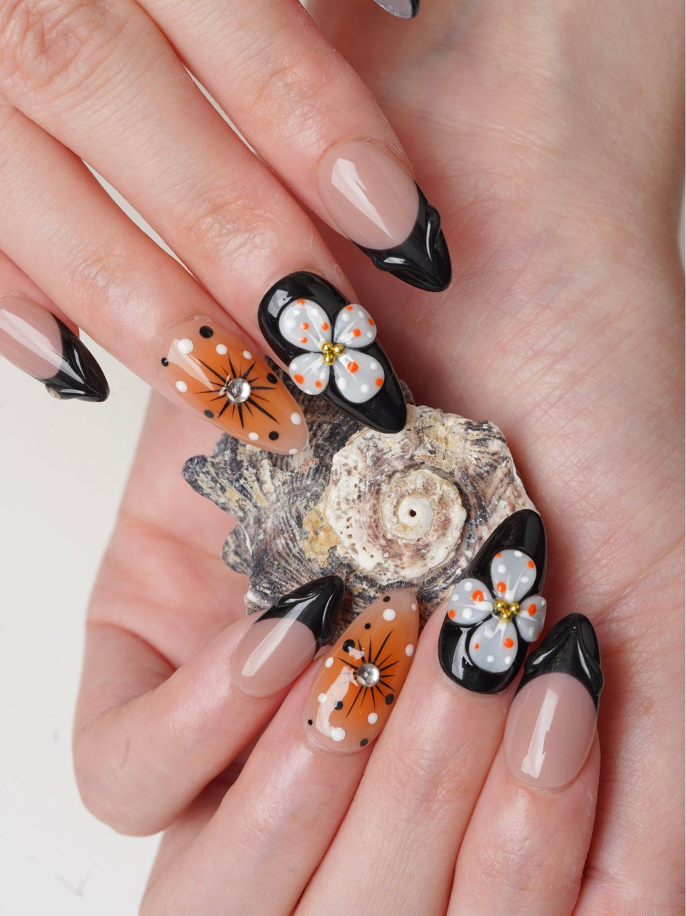 Handmade floral nails featuring orange petals, polka dots, and glossy nude-black accents