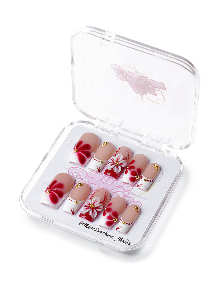 Square nails with red and white 3D flowers, gold gems, and nude base