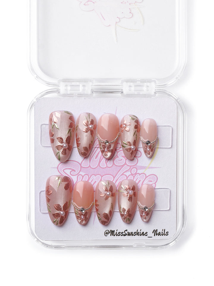 Elegant blush press-on nails featuring floral designs and vintage-inspired pearl and chain details.