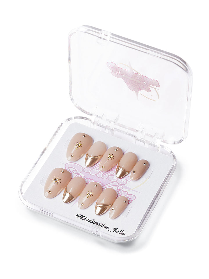 Short almond nude press-on nails with gold chrome tips and metallic star embellishments