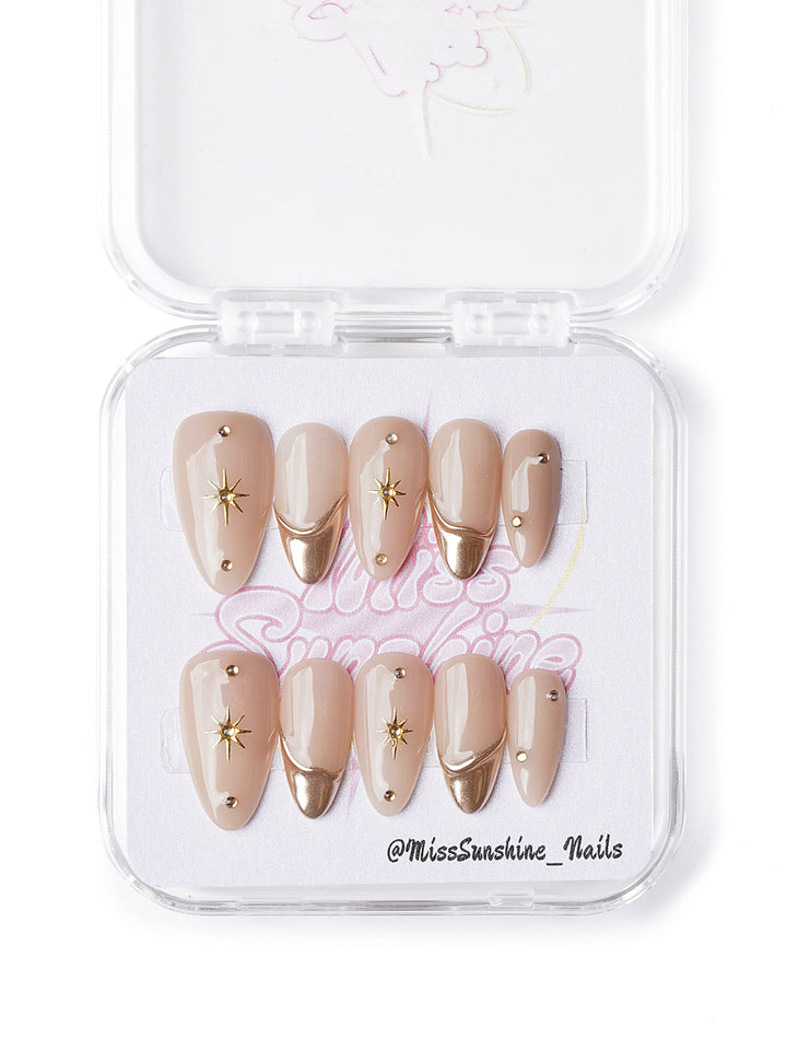Handmade short almond nails with nude base, gold accents, and celestial star charms
