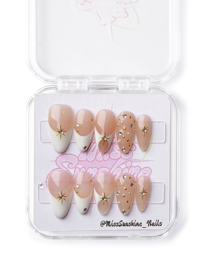 Elegant nude and white press-on nails with gold starbursts and subtle shimmer for a radiant look.