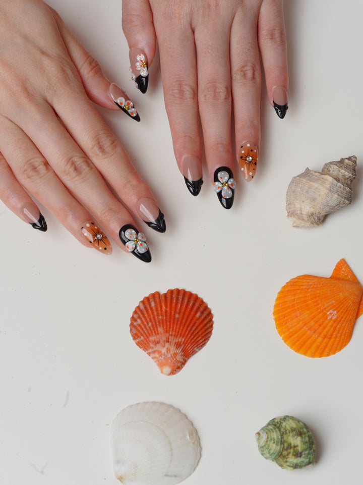 Short almond press-on nails with 3D orange flowers, black French tips, and nude base