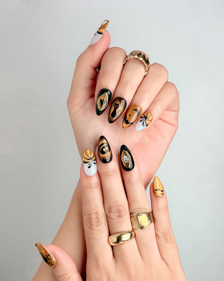 Cute Halloween press-on nails with pumpkin, black cat, bat, and ghost designs in orange, black, and white.