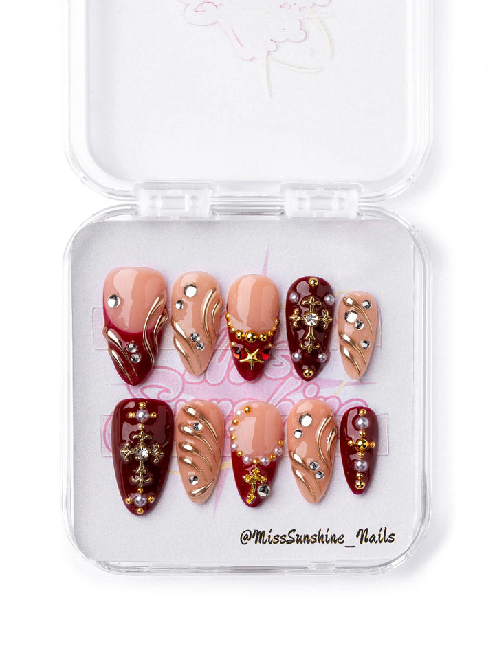 Ruby Saint press-on nails with ruby red accents, gold charms, and rhinestones