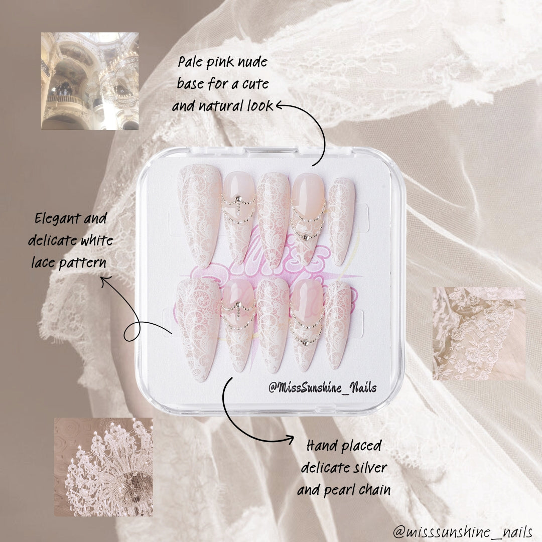 Long almond blush nails featuring intricate white lace patterns and delicate crystals