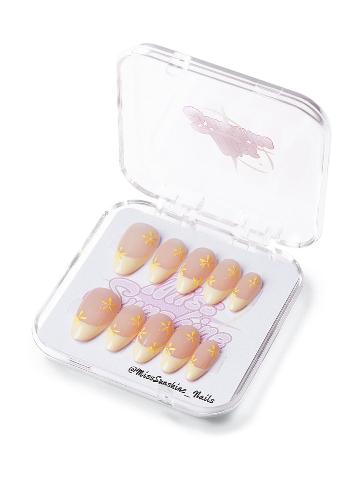 Short almond press-on nails with pale yellow French tips and hand-painted daisy petals